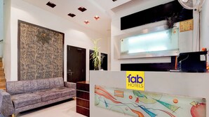 A hotel reception area with a sofa, a wall with abstract art, and a reception desk with a logo. - Via Paradise Stay Inn (Mawal)