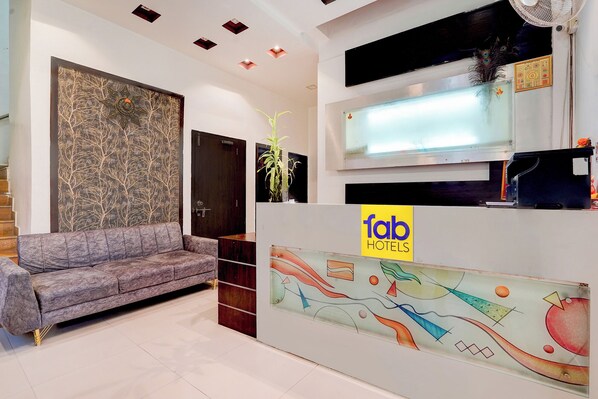 A hotel reception area with a sofa, a wall with abstract art, and a reception desk with a logo. - Via Paradise Stay Inn (Mawal)