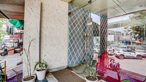Entrada de hotel com parede azulejada, plantas em vasos e vista para a rua.