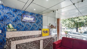 Uma área de recepção com parede de mosaico azul, um quadro com cavalos, um balcão de recepção e um sofá vermelho.