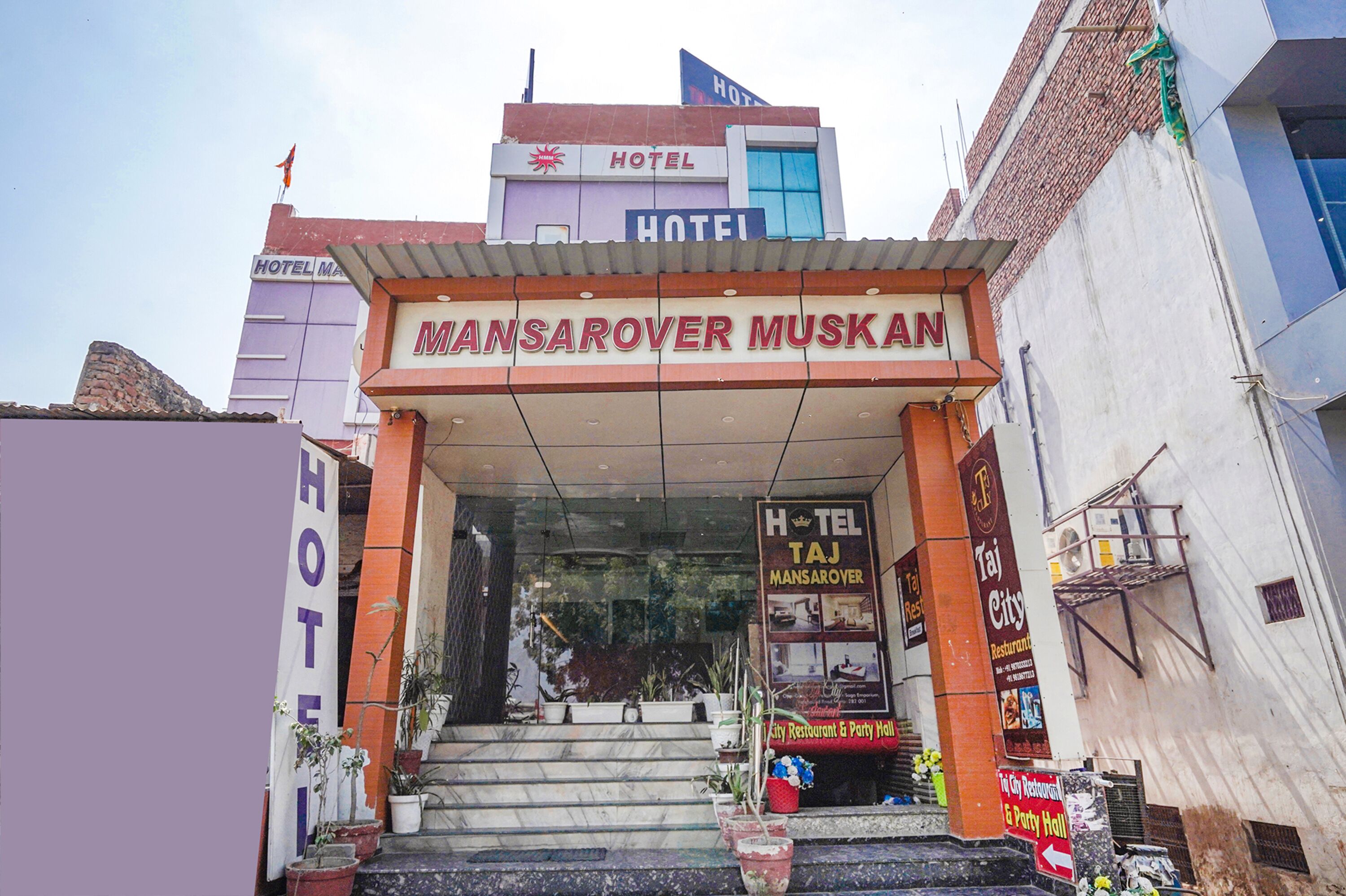The entrance to Mansarover Muskan hotel with a signboard and potted plants.