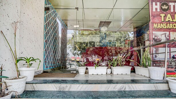 Entrada de hotel com degraus de mármore, plantas em vasos e porta de vidro.
