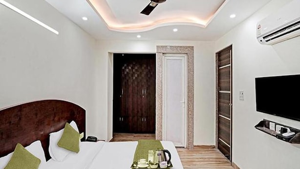 A modern hotel room with a bed, a TV, and a ceiling fan. - Fabhotel Bellmore Stay & Homes (Gurugram)