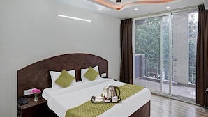 A hotel room with a large bed, a nightstand, a tray with breakfast items, and a view of the outdoors. - Fabhotel Bellmore Stay & Homes (Gurugram)