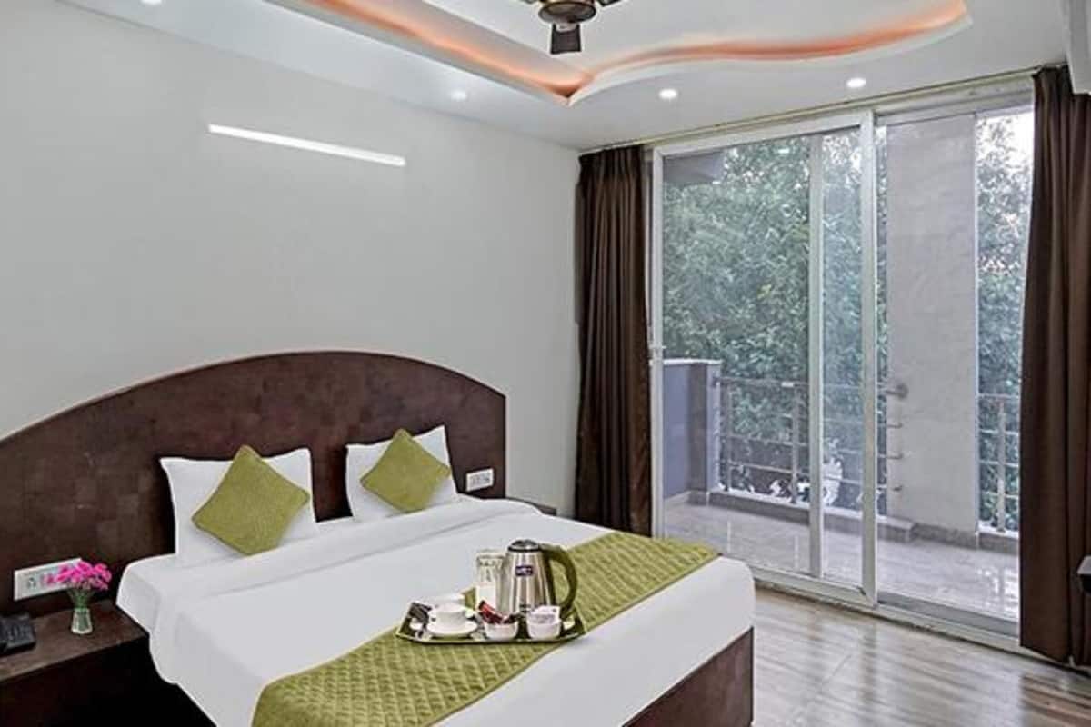 A hotel room with a large bed, a nightstand, a tray with breakfast items, and a view of the outdoors.