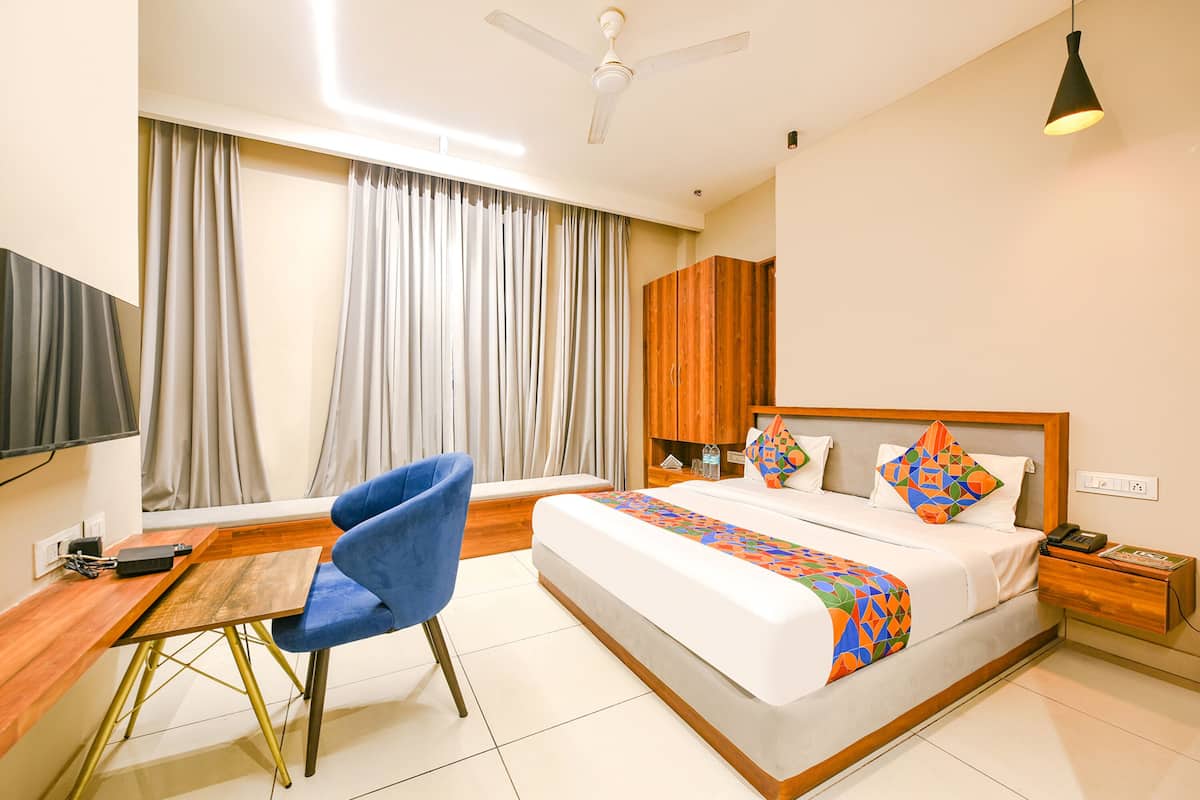 Una habitación de hotel con cama, escritorio, silla, televisor, ventilador de techo y mesita de noche.