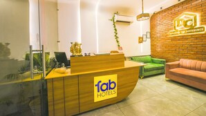 Een hotel receptie met een houten balie, een groene bank en een bakstenen muur met een logo.