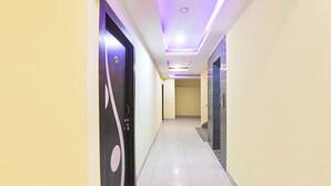 A hallway with a modern design, featuring a black door with a circular design, a tiled floor, and a ceiling with recessed lighting. - Fabhotel Magadh Regency (Patna)