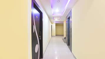 A hallway with a modern design, featuring a black door with a circular design, a tiled floor, and a ceiling with recessed lighting.