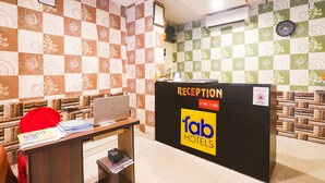 A reception desk with a laptop, a red bag, and some documents. The wall has a checkered pattern with floral designs. - Fabhotel Magadh Regency (Patna)