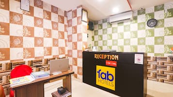 A reception desk with a laptop, a red bag, and some documents. The wall has a checkered pattern with floral designs.
