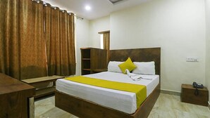 Une chambre d’hôtel avec un grand lit, une tête de lit en bois, une table de chevet, une commode, un miroir et une armoire.