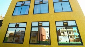 Un bâtiment jaune doté de nombreuses fenêtres, dans lequel on peut distinguer le reflet d’autres bâtiments.