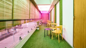 A corridor with a glass railing, green artificial grass, and yellow chairs.