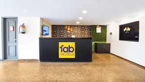 A reception area with a 'fab hotels' sign, a fire extinguisher, a television, and a green wall with a security camera. - Fabhotel The Luxe Inn (New Delhi)
