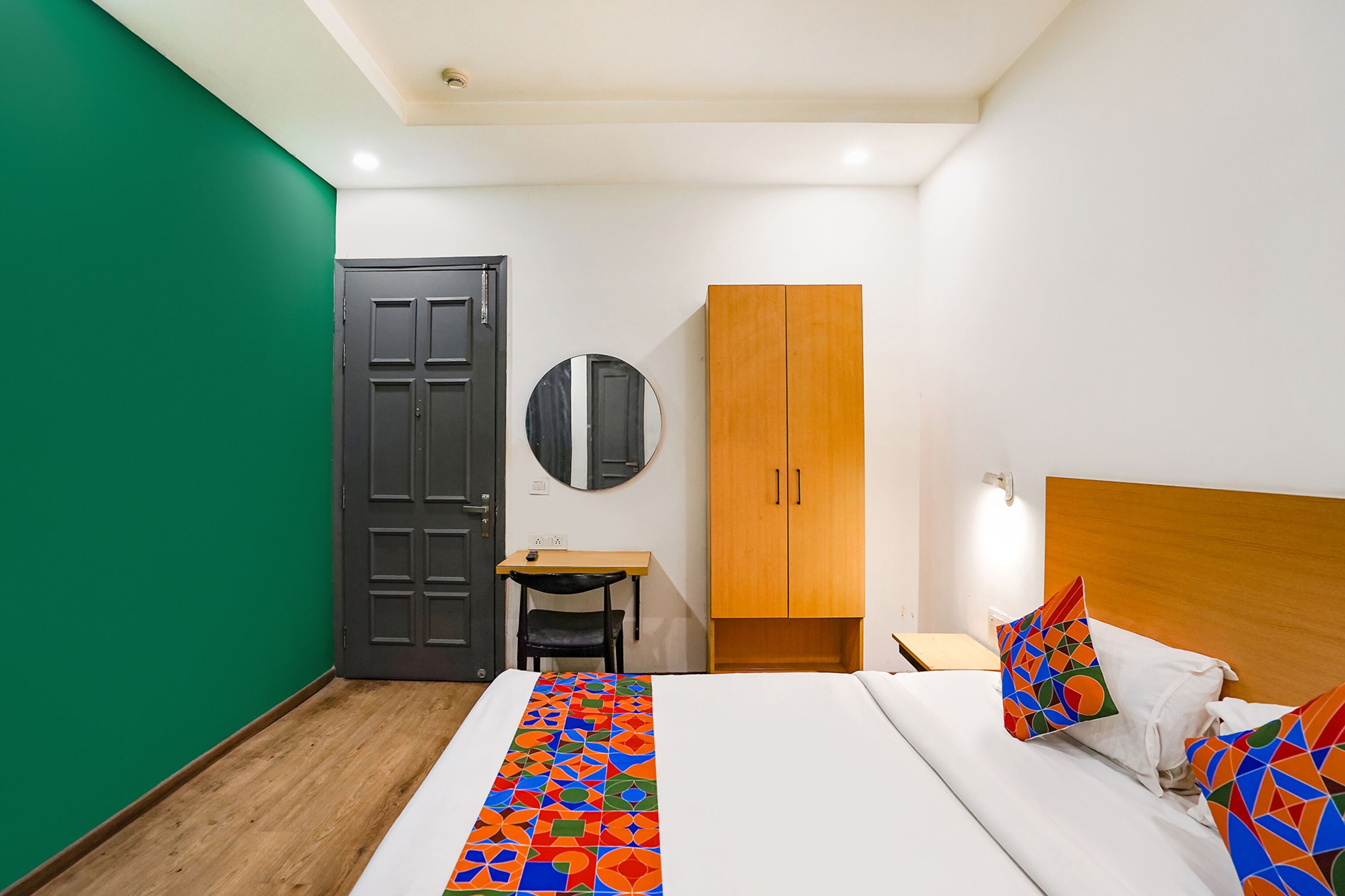 A bedroom with a bed, a desk, a chair, a wardrobe, and a mirror.