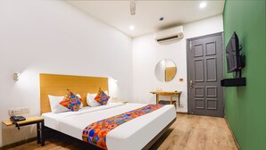 A hotel room with a bed, bedside table, wall-mounted TV, and a green wall. - Fabhotel The Luxe Inn (New Delhi)