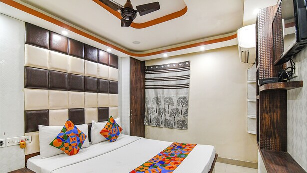 Habitación de hotel con una cama grande, ventilador de techo, televisión y ventana con cortina.