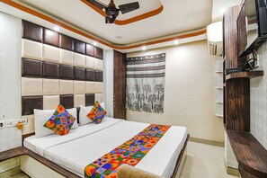 Habitación de hotel con una cama grande, ventilador de techo, televisión y ventana con cortina.