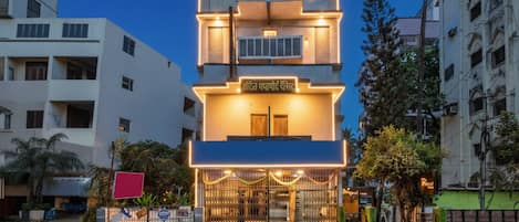Un hotel de varios pisos con fachada moderna, señalización iluminada y entrada protegida por una reja.