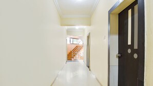 A hallway with a dark door on the right, a staircase at the end, and a light-colored floor. - Via Yashraj Inn (Pune)