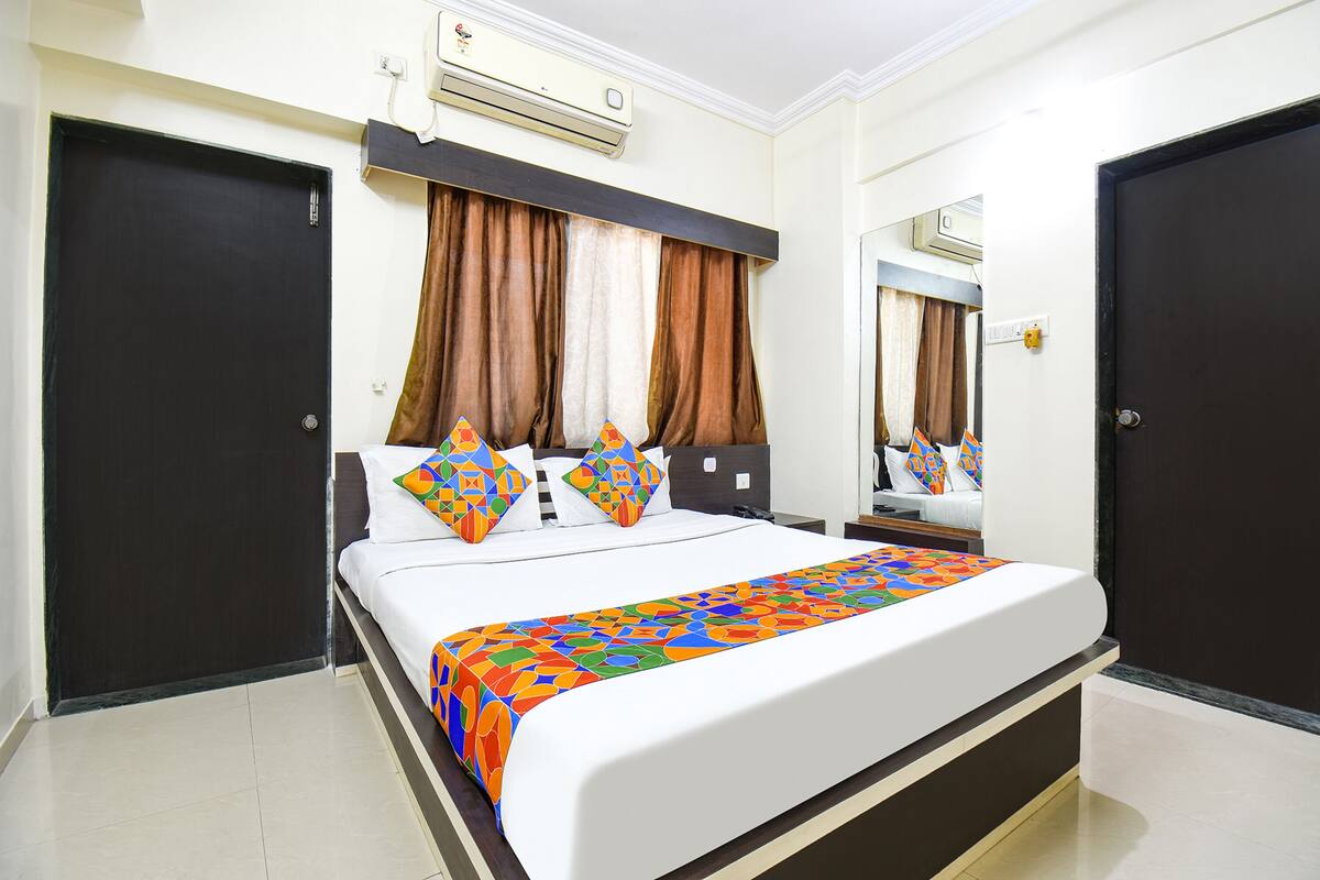 A hotel room with a bed, air conditioning unit, curtains, and a mirror.