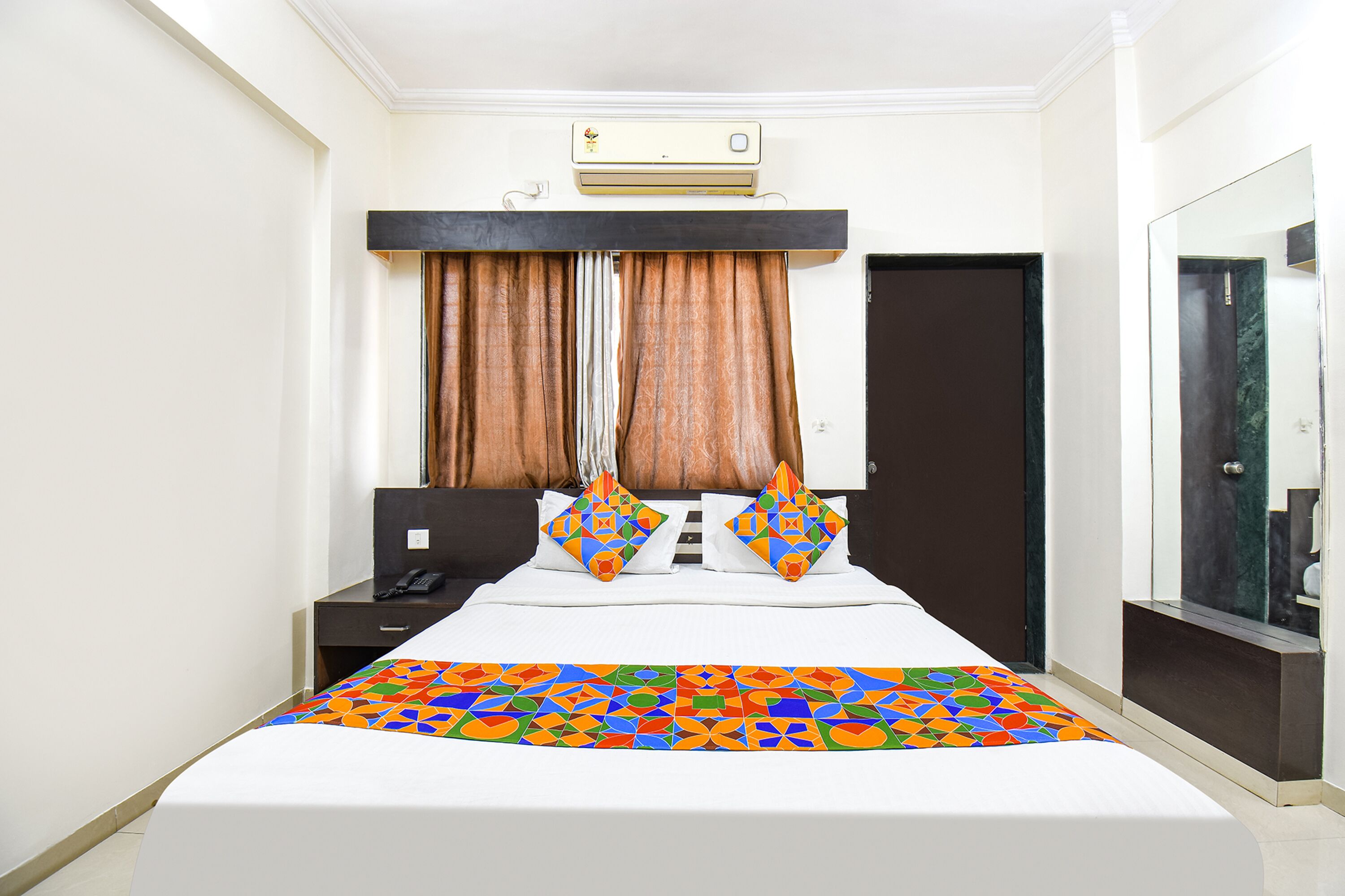 A hotel room with a bed, a desk, a telephone, and a mirror.