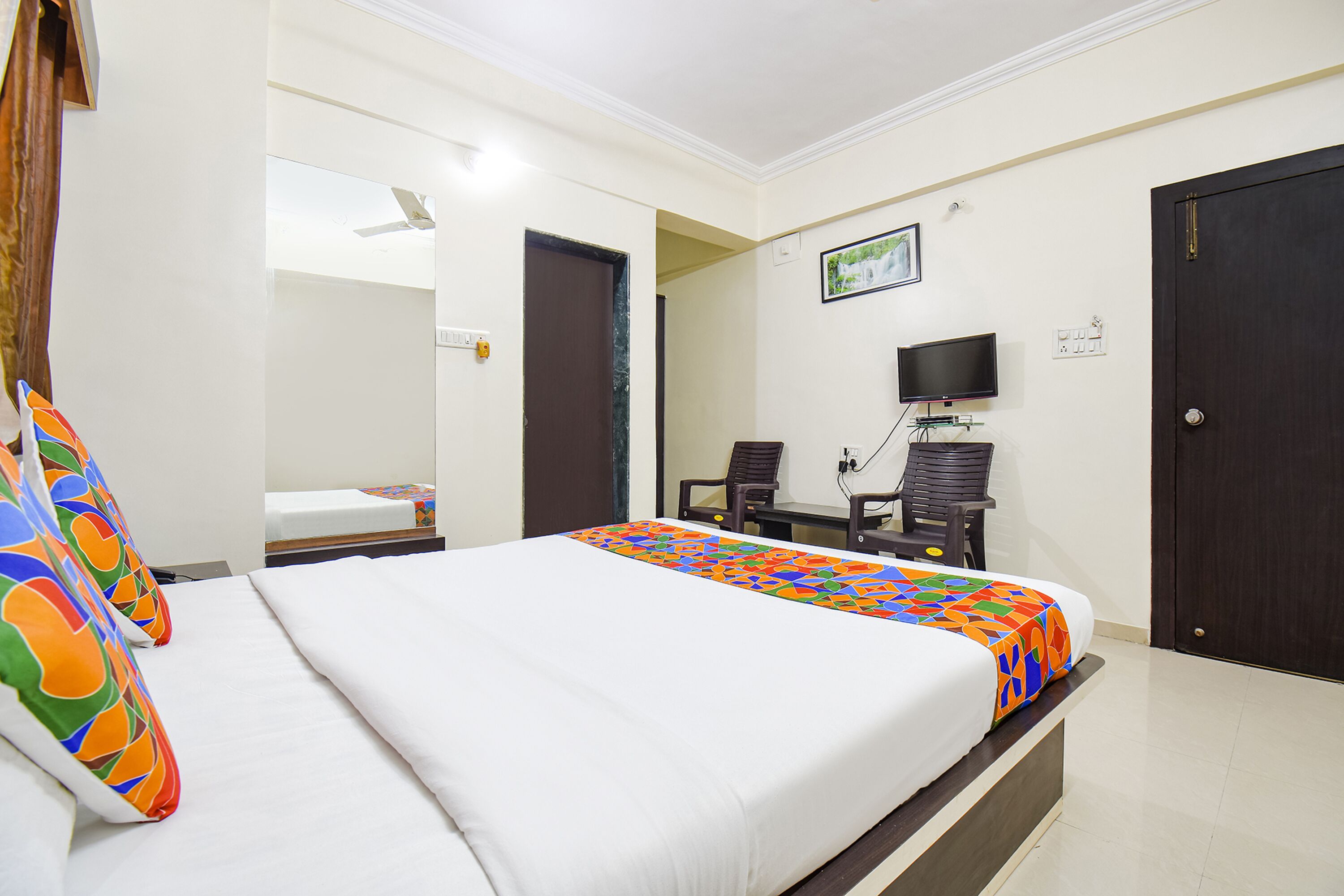A hotel room with a bed, a desk with a chair, a television, and a door.