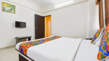 Una cama bien hecha con un edredón colorido, un televisor de pantalla plana sobre un mueble, y una puerta que da a otra habitación.