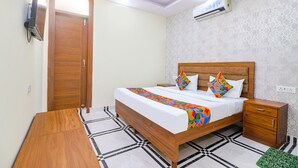 A bedroom with a wooden bed, a nightstand, a TV, and an air conditioning unit. - Fabhotel Starlight (New Delhi)