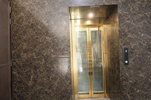 An elevator with a glass door and a control panel on the wall. - FabHotel Moody Inn Kalkaji (New Delhi)