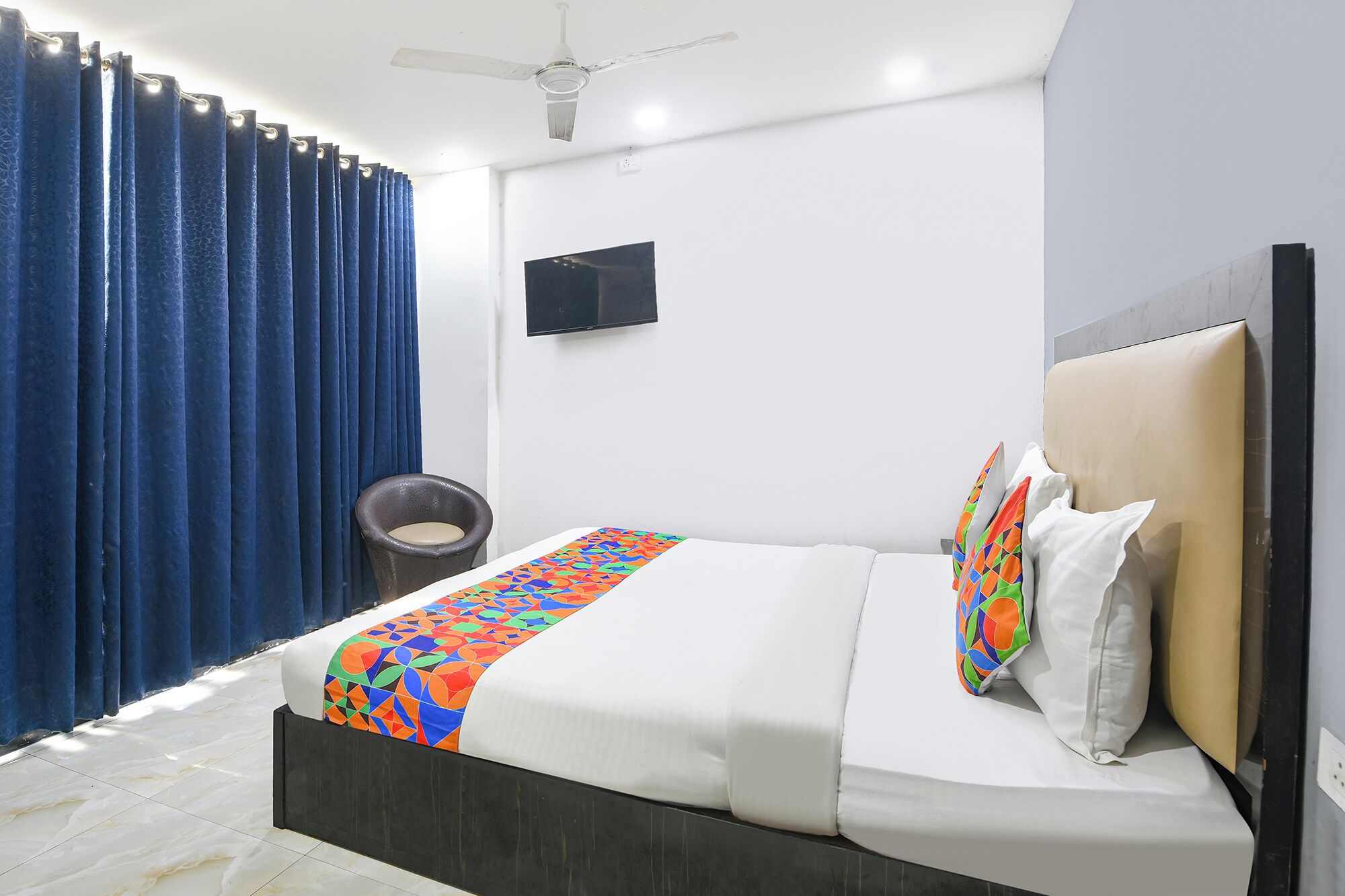 A bedroom with a bed, a chair, a ceiling fan, and a TV on the wall.
