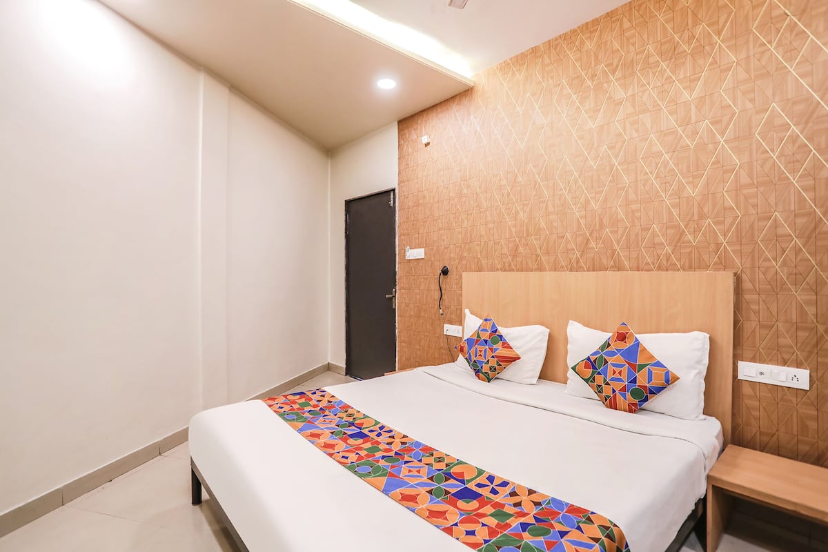Habitación de hotel con cama, cabecera de madera, mesita de noche y corredor de cama con estampado geométrico.