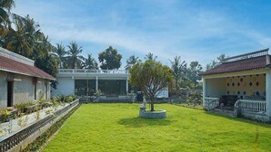 A courtyard with a lawn, a small tree, and two buildings with red-tiled roofs. - FabHotel Prime Indeedcare (Kakdwip)