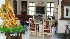 A living room with a large golden statue, a sofa, a TV, and a small table with chairs. - FabHotel Prime Indeedcare (Kakdwip)