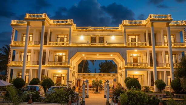 A large, multi-story building with a central archway, multiple balconies, and a well-lit entrance. - FabHotel Prime Indeedcare (Kakdwip)
