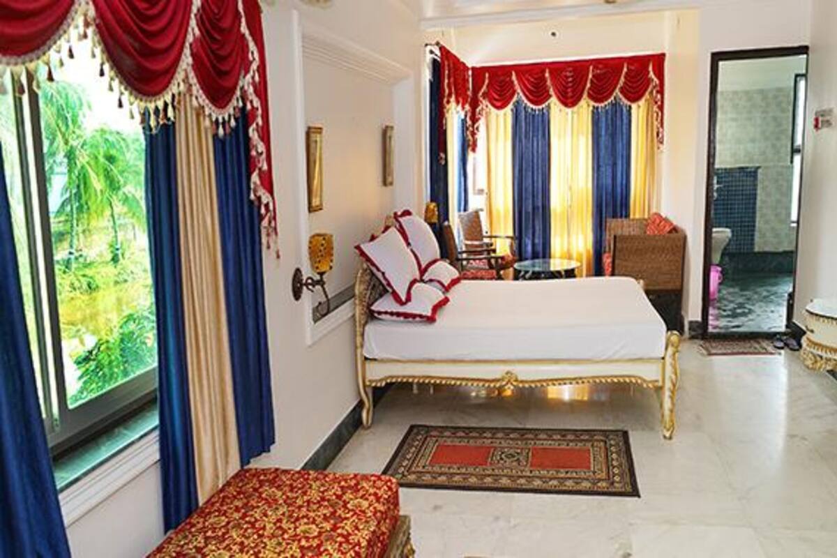 A spacious bedroom with a large bed, a sitting area with a table and chairs, and a view of greenery outside.