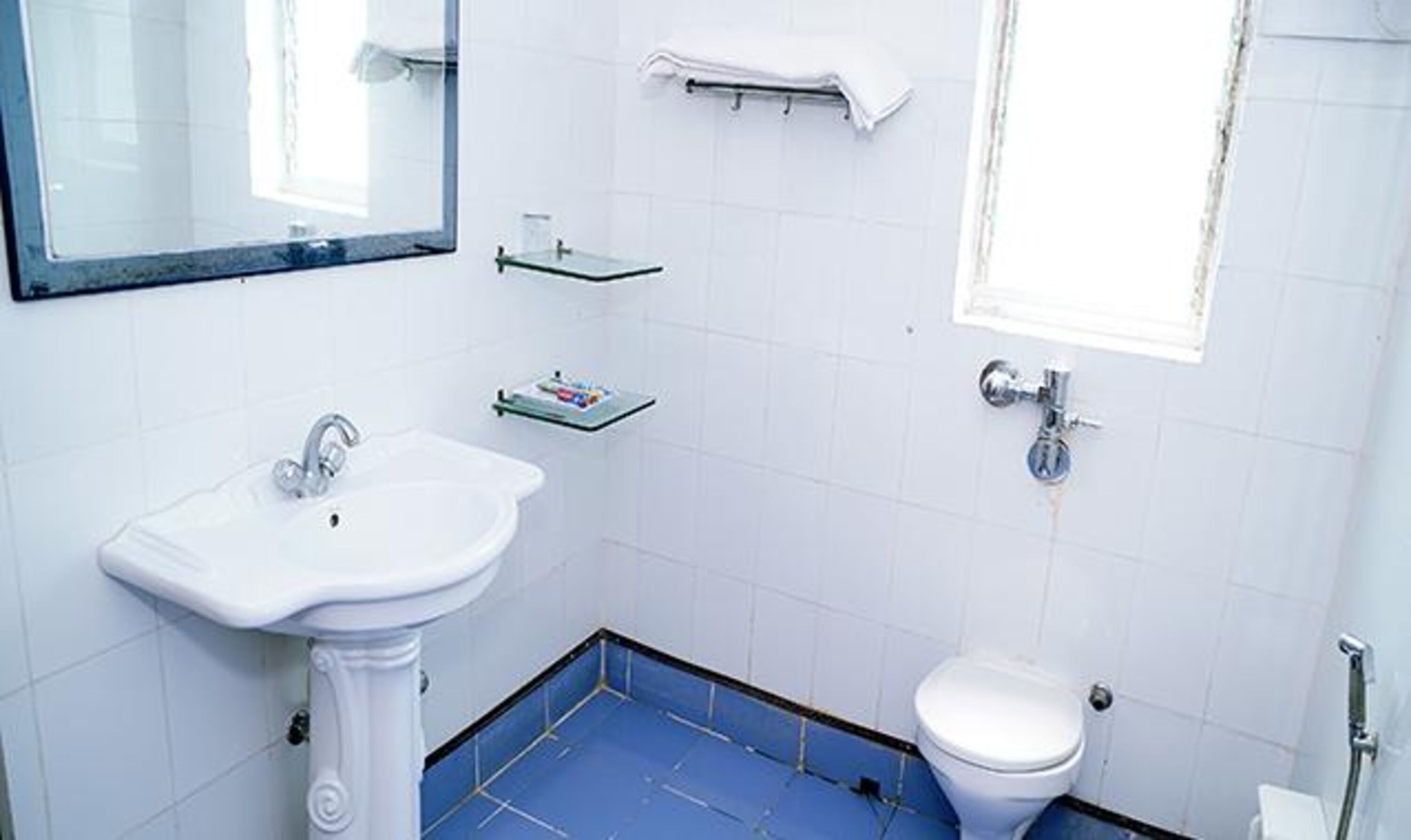 A bathroom with a pedestal sink, a toilet, and a small window.