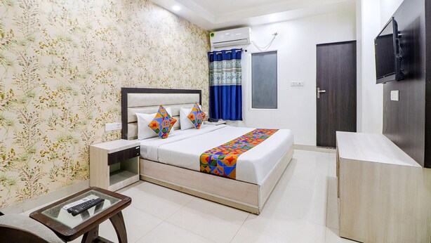 A hotel room with a bed, bedside tables, a TV, and a ceiling fan. - Fabexpress Gross Aero (New Delhi)