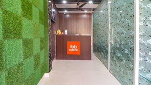 A reception area with a wooden counter, a 'fab express' sign, and a green wall with a checkered pattern. - Fabexpress Gross Aero (New Delhi)