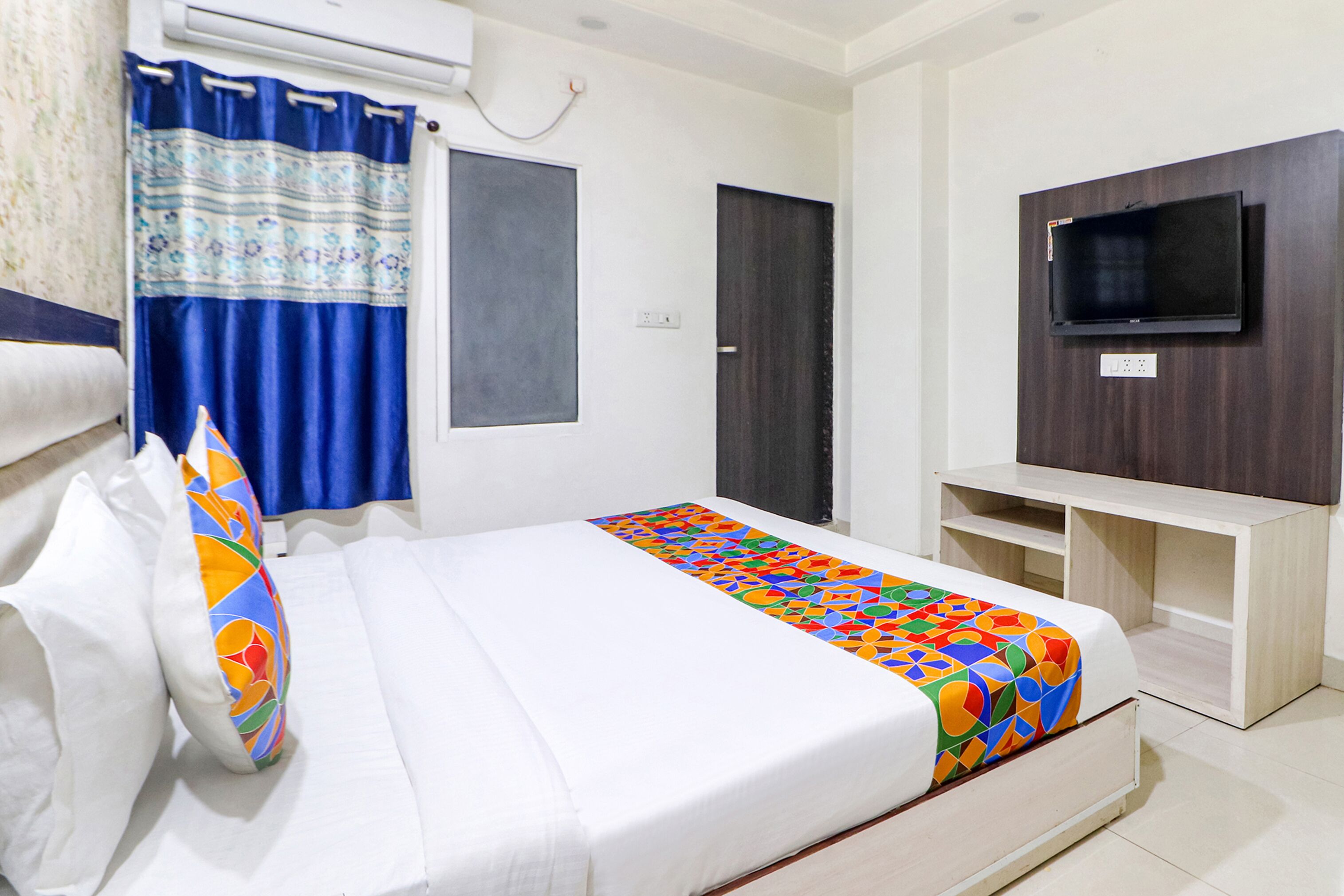 A hotel room with a bed, a TV mounted on the wall, a wardrobe, and a curtain.