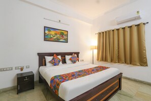 A neatly made bed with a colorful bedspread, a nightstand with a drawer, a wall-mounted air conditioner, and a painting above the bed. - Fabhotel Sv Orchids Jubilee Hills (Hyderabad)