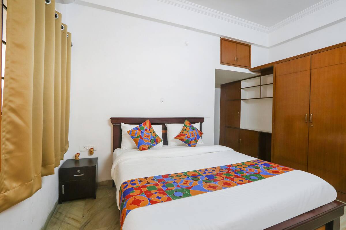 A neatly made bed with a colorful geometric-patterned bedspread, a wooden headboard, and a small bedside table with a lamp.