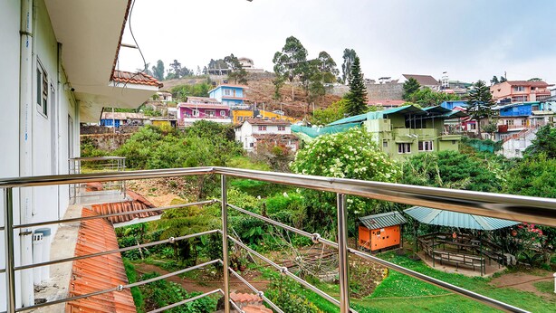 Ein Balkon mit Metallgeländer, der auf einen Wohnbereich mit bunten Häusern und viel Grün blickt.