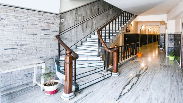 Un escalier avec des rampes en bois et des marches en marbre, menant à un palier agrémenté d’un banc et de plantes en pot.