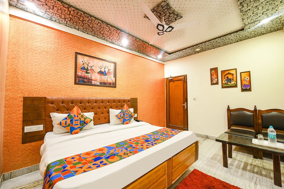 Una habitación de hotel con una cama grande, cabecera de madera, alfombra roja, una mesita de cristal con una botella de agua y un ventilador de techo.
