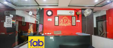 A hotel reception area with a red wall, a clock, and a fan.