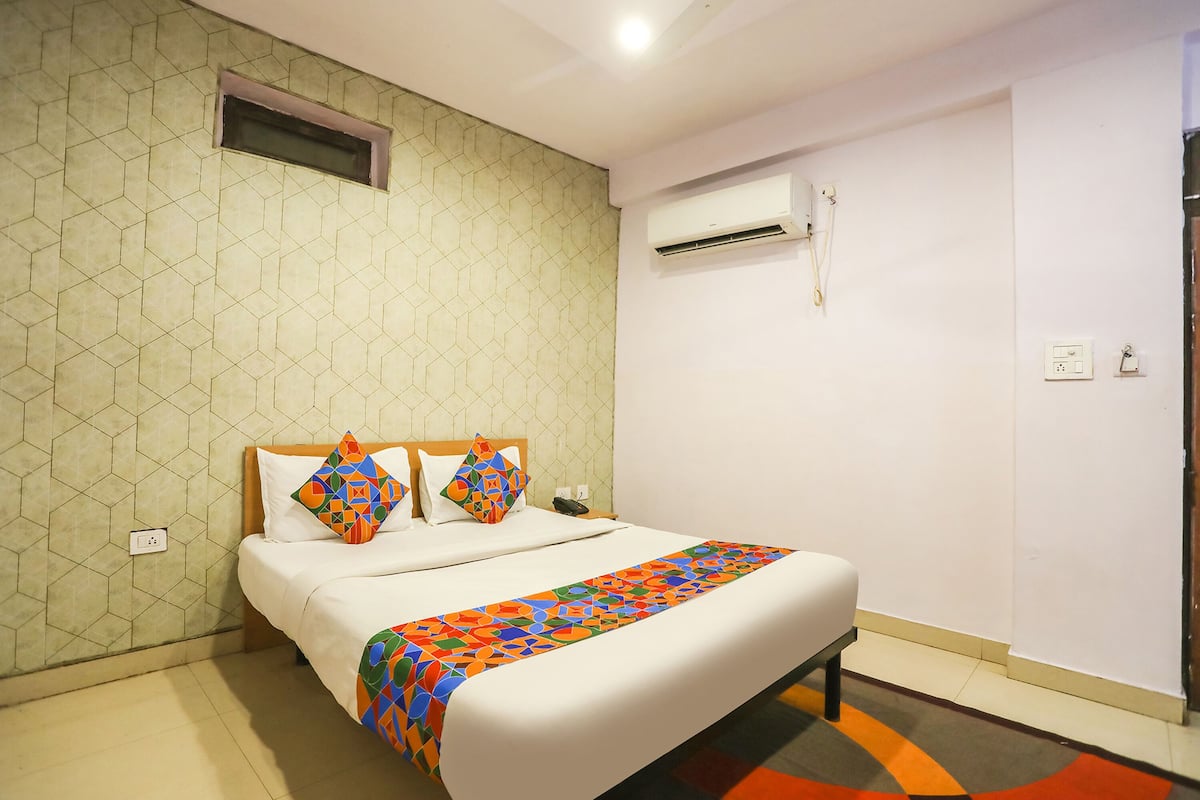 A hotel room with a bed, a patterned wall, an air conditioning unit, and a door.
