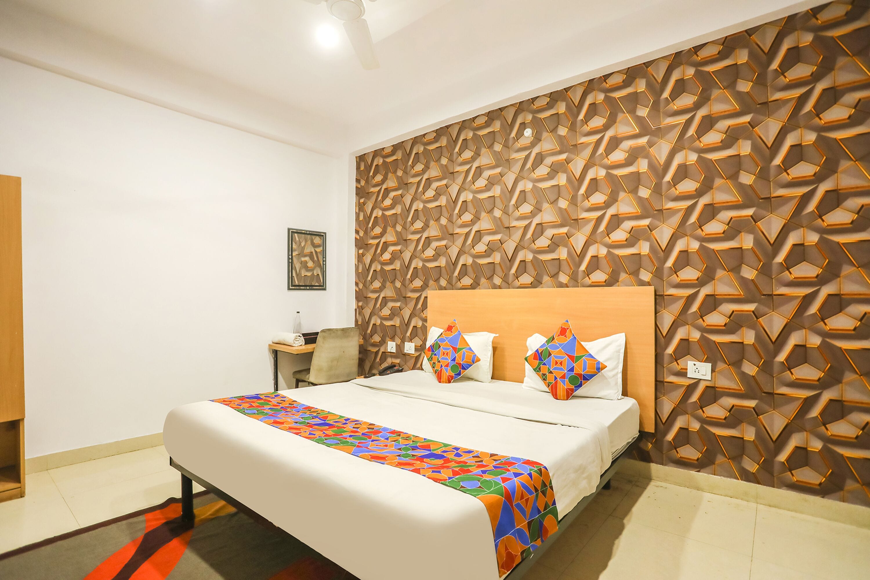 A hotel room with a bed, a nightstand, a wall with a geometric pattern, and a ceiling fan.
