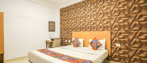 A hotel room with a bed, a nightstand, a wall with a geometric pattern, and a ceiling fan.